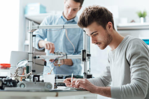 51422799 - engineering students working in the lab, a student is using a 3d printer in the background